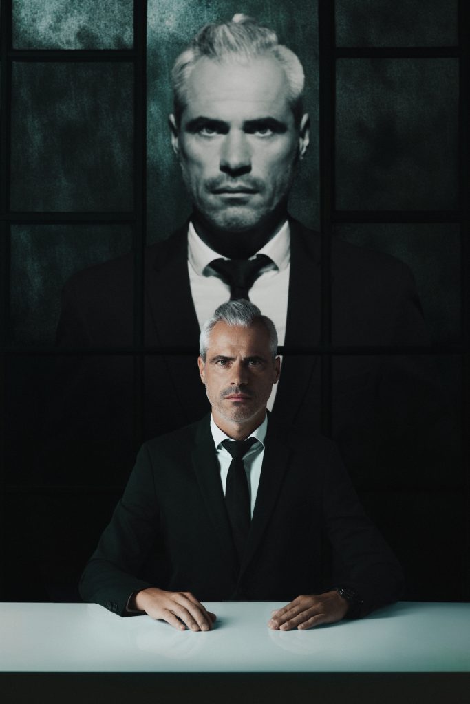 Man sieht ein Bild wo zweimal der gleiche Mann darauf zu sehen ist, einmal in Farbe und einmal in schwarz-weiß, beide schauen mit ernster Miene in die Kamera